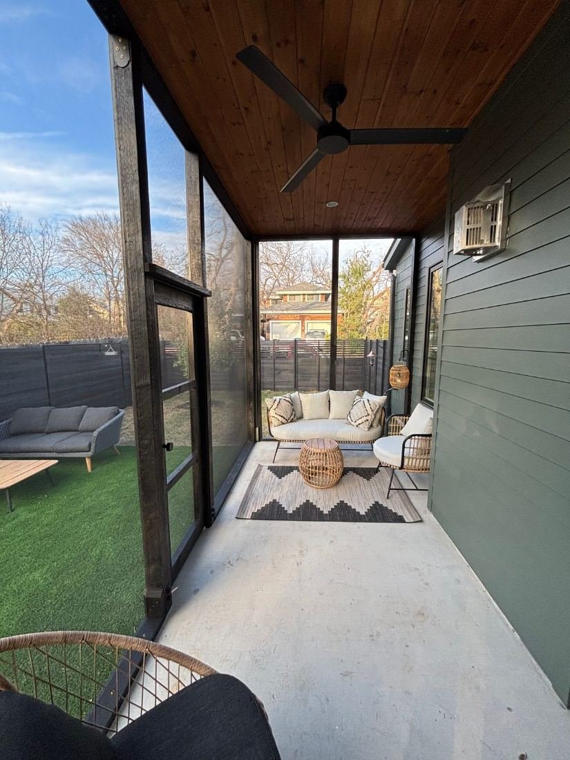 Covered porch screened in with black-framed panels and a hand-built door, cedar plank ceiling above, furnished with a sofa and rug, golden evening light