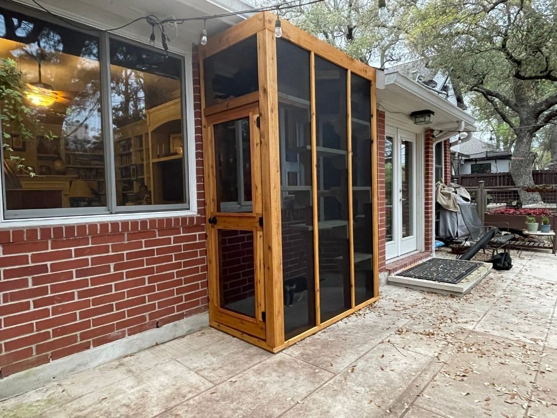 Taller cedar-framed window catio standing floor to eaves against a brick wall beside a patio door