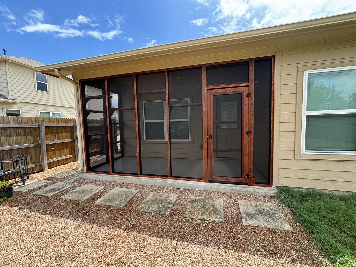 A back patio enclosed with cedar-framed screen panels and a matching screen door, shelving visible inside