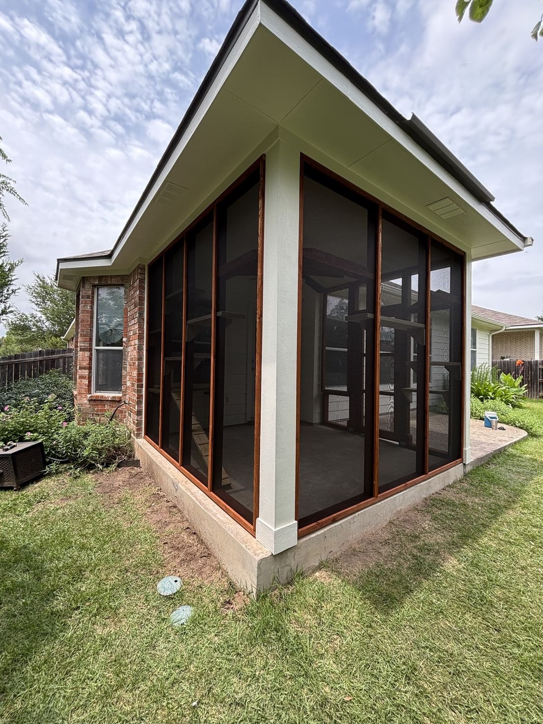 A patio corner enclosed in cedar-framed black screening under a wide eave, shelves running the inside walls