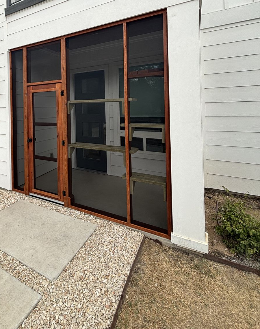 A cedar-framed screened entry catio with a handmade screen door and wood climbing shelves, built into the front of a modern white home